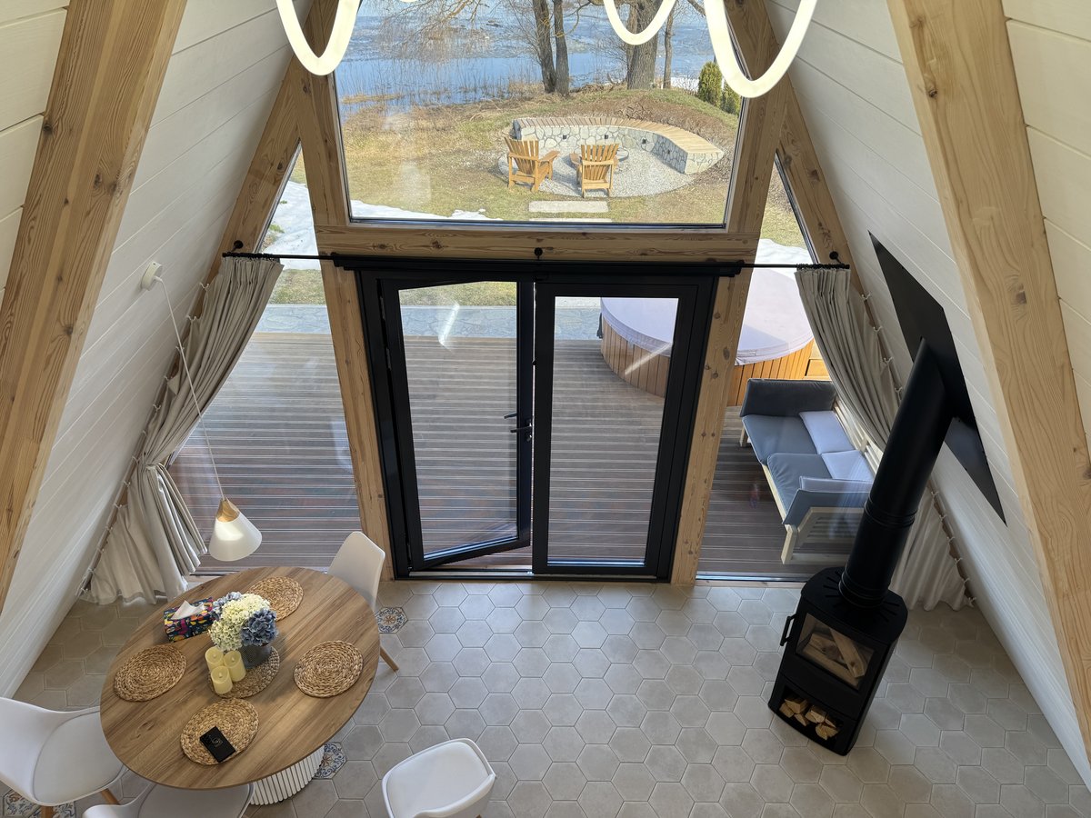 Интерьер A-frame с панорамным окном, обеденным столом, диваном и дровяной печью, вид на костёр и купель